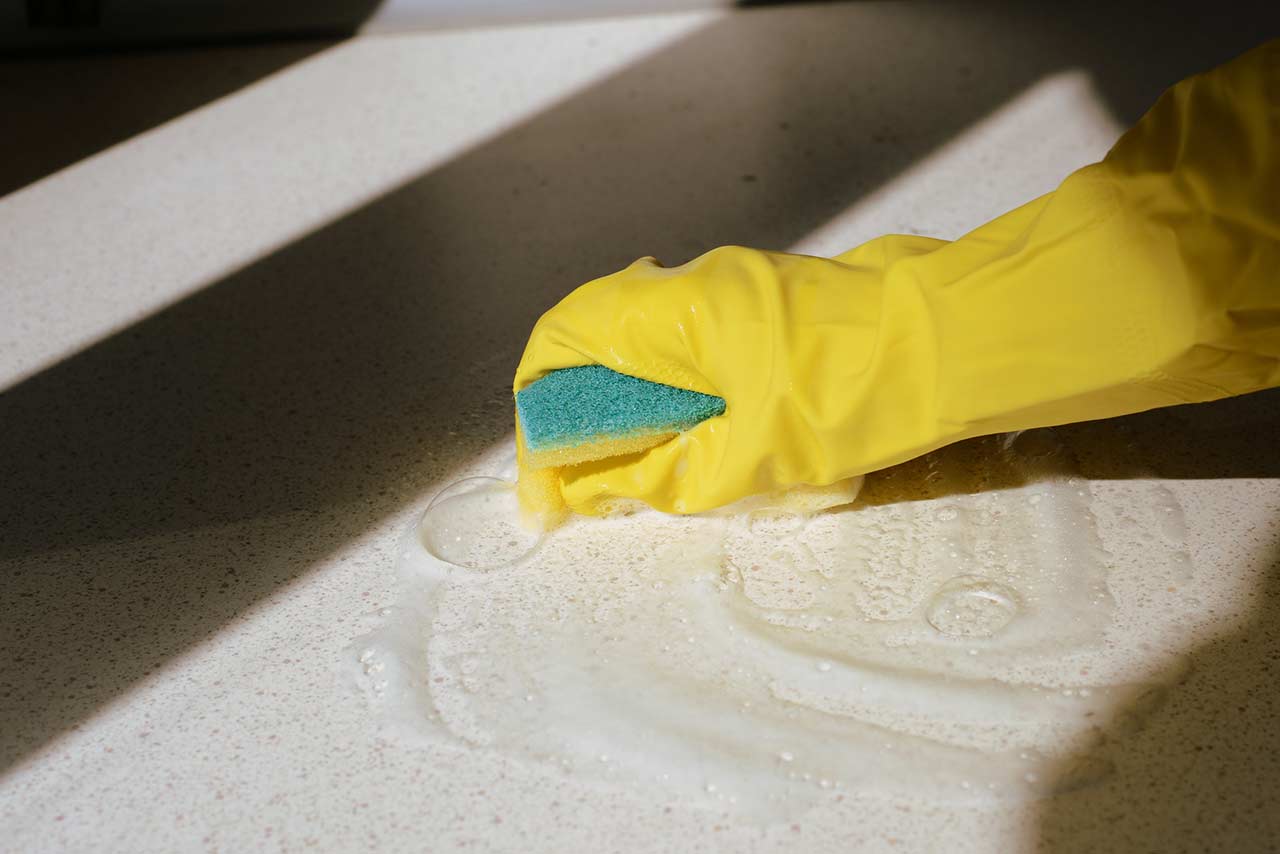After reading how to clean granite countertops, person cleans granite countertops with soap, water and sponge. 
