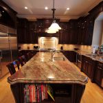 featured image on a blog regarding countertop edge profiles. This image depicts a kitchen with dark wood cabinetry and a long island in the middle with a granite countertop