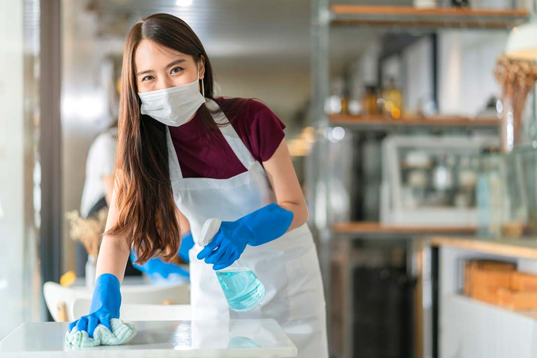 Picture of a smiling woman disinfecting quartz countertops and tables at a café.