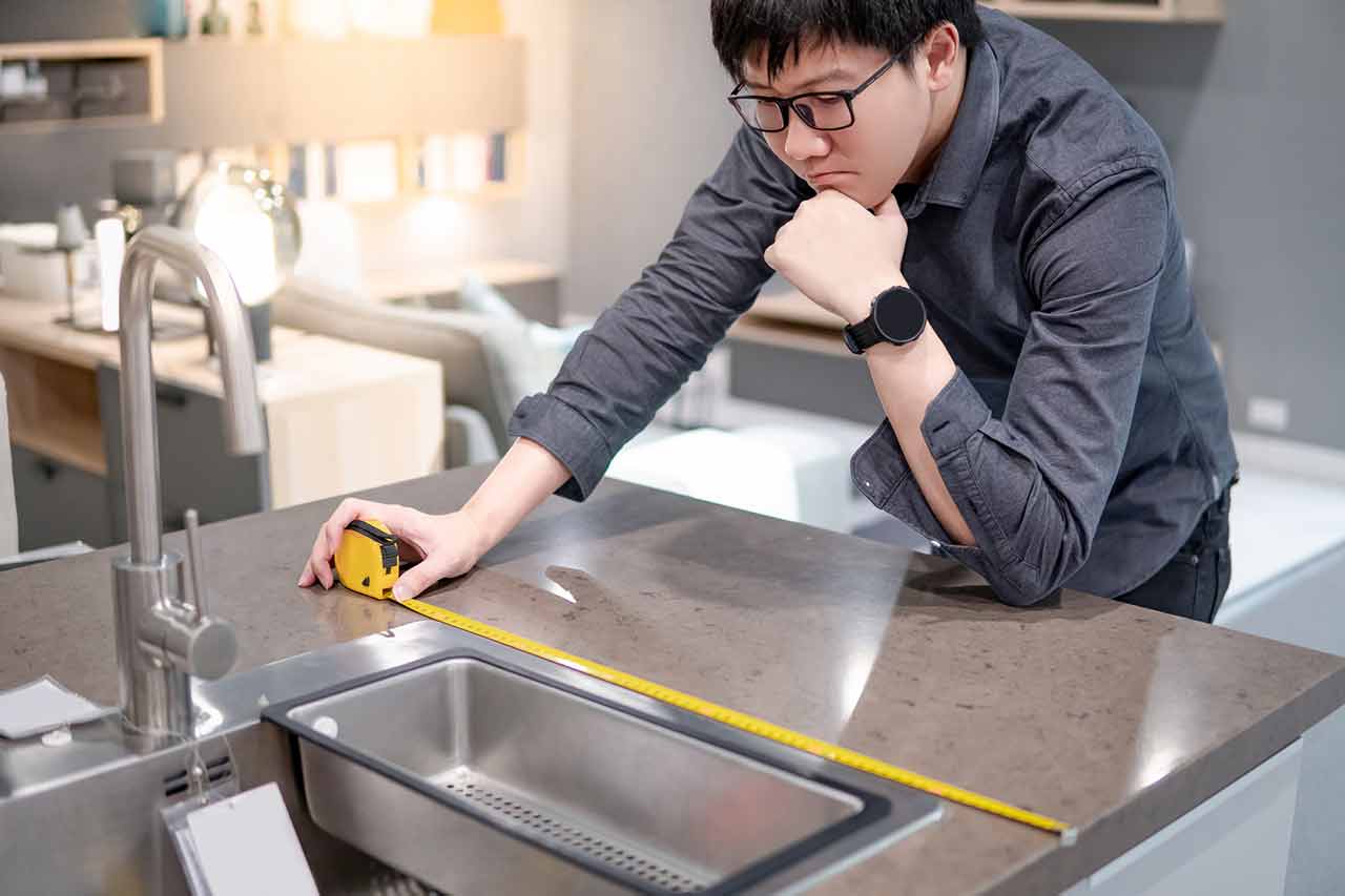 Person holding a tape measure on cheap granite countertops wondering if he could do granite fabrication and granite installation by himself.